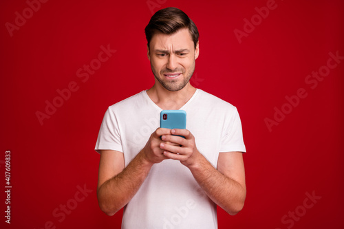 Photo portrait of young man unhappy stressed reading fake news cellphone biting lip isolated vibrant red color background