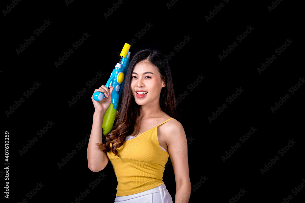 Portrait cheerful young asian woman Wearing a yellow tank top ,holding plastic water gun Smiling and having fun playing in the water Songkran festival, Songkran Thailand. isolated on black background. Portrait cheerful young asian woman Wearing a yellow tank top ,holding plastic water gun Smiling and having fun playing in the water Songkran festival, Songkran Thailand. isolated on black background.