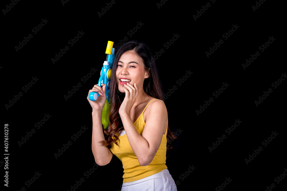 Portrait cheerful young asian woman Wearing a yellow tank top ,holding plastic water gun Smiling and having fun playing in the water Songkran festival, Songkran Thailand. isolated on black background.