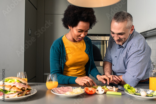 Mid adult couple standing in the kitchen preparing sandwich for breakfast at home.