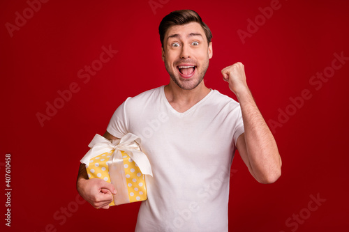 Photo of delighted guy fist up open mouth arm hold x-mas giftbox isolated on maroon color background