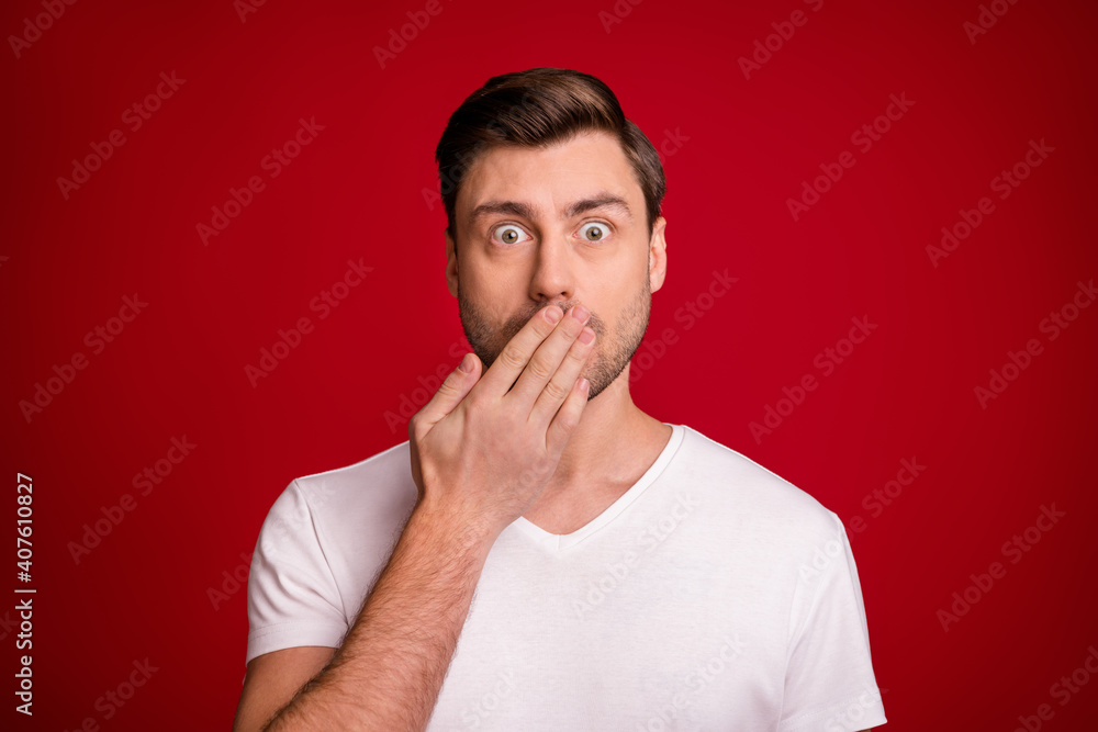 Photo portrait of shocked surprised guy keeping secret closed mouth with hand staring isolated vibrant red color background
