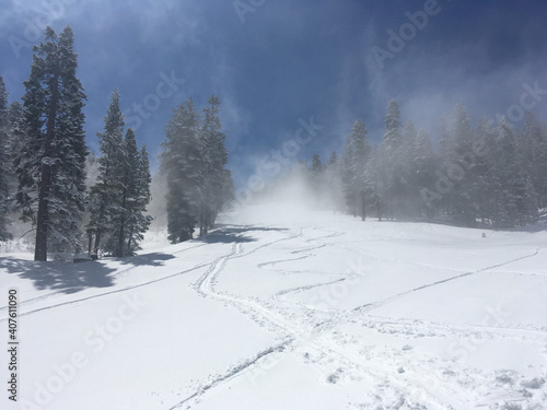 Scenic landscape view of the fog rolling onto a mountain covered in snow, ski and snowboard track, framed by pine trees.