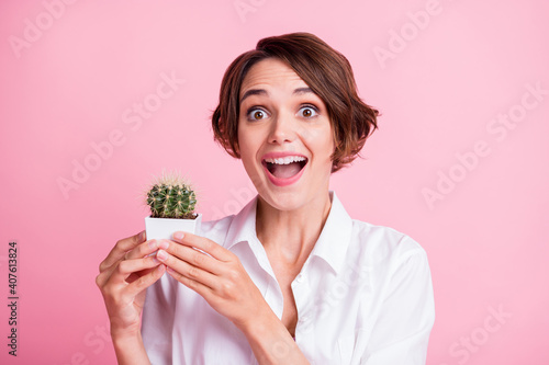 Photo of astonished girl holding cactus open mouth unbelievable grow isolated on pink color background