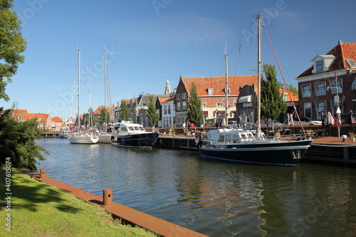 Historic houses in Enkhuizen, West Friesland, Netherlands, with mooring sailing boats and the tower of Zuiderkerk (or St Pancraskerk) in the background