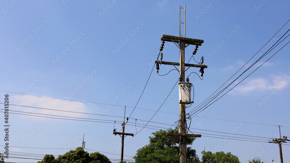 Transformer on pole. Single phase transformer with fuse for converting high voltage to low voltage and wires on pole has green tree background with blue sky with copy space. Selective focus