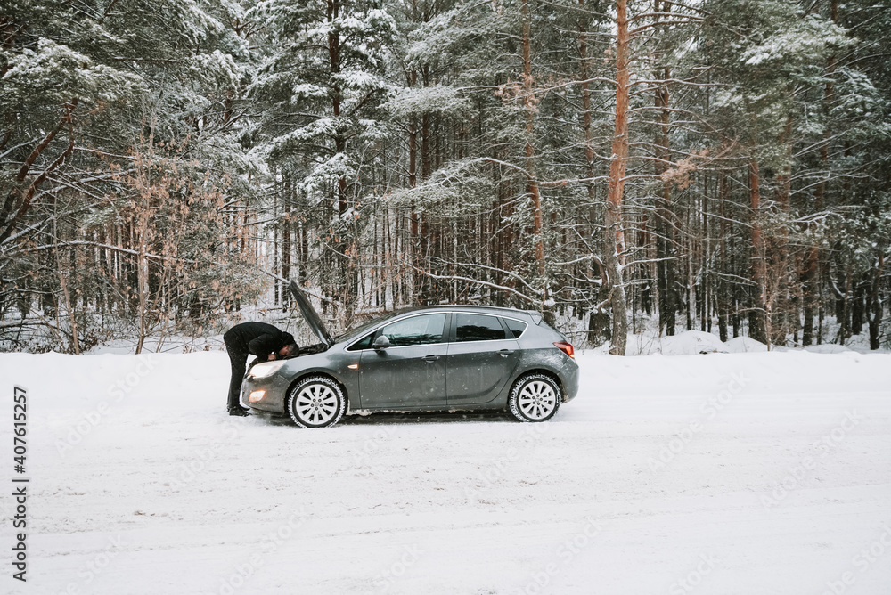 A car with an open hood on the background of a winter forest