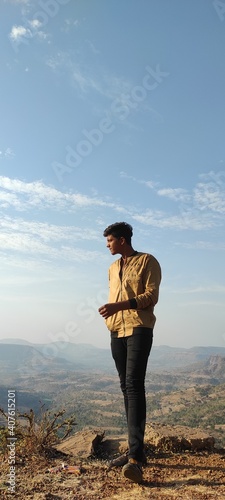 A young boy standing on the top of the hill under blue sky
