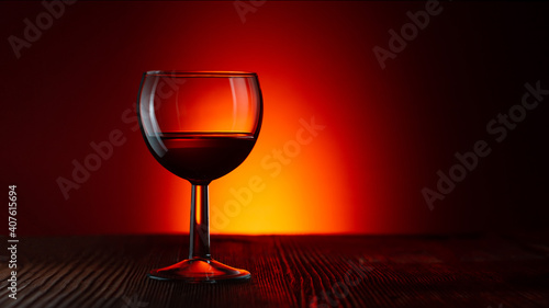 A glass of red wine stands on a wooden table against a dark illuminated background