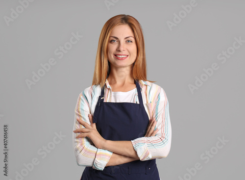 Canvas Print Beautiful young woman wearing apron on grey background