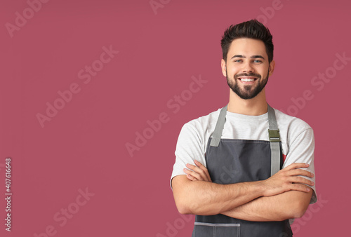 Young man wearing apron on color background photo