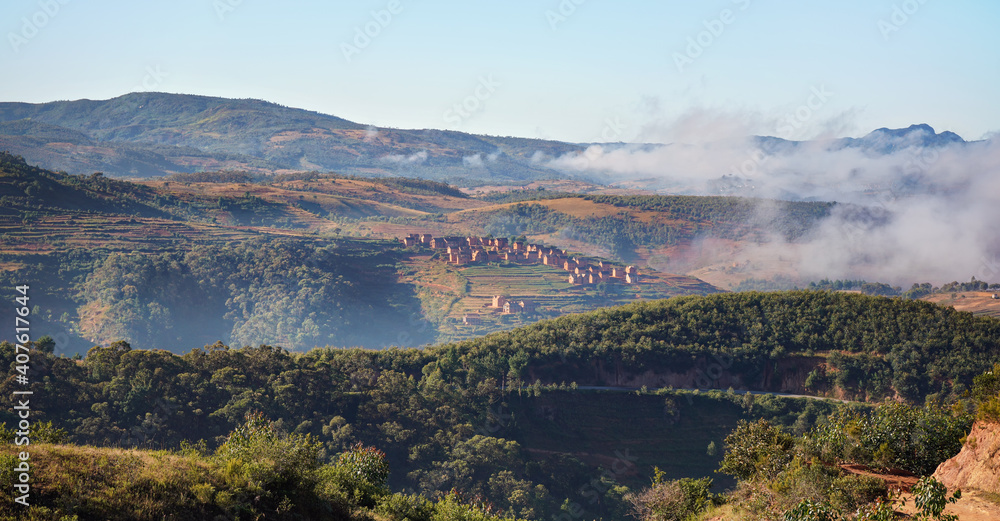 Fog over valley with small village on sunny morning in region near Alakamisy Ambohimaha, Madagascar