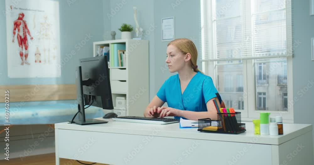 Portrait of beautiful female nurse working on computer in hospital office room. Young Caucasian woman typing and looking at camera in clinic. Healthcare, profession, pandemic concept. Portrait of beautiful female nurse working on computer in hospital office room. Young Caucasian woman typing and looking at camera in clinic. Healthcare, profession, pandemic concept.