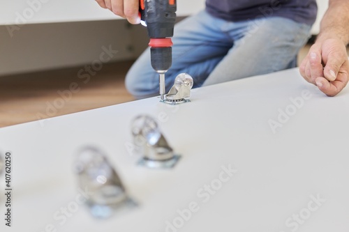 Furniture wheels close-up. Worker hands assembling furniture using professional tool