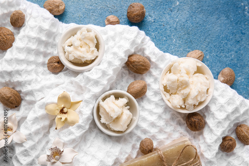 Bowls with shea butter and towel on color background