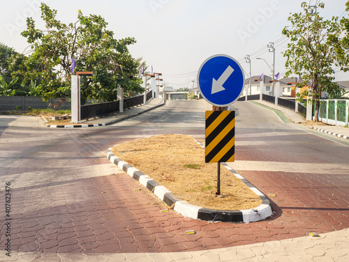 left lane signpost a white arrow on blue circle plate at center of village street for drive safety warnig to road direction navigation before cross the bridge photo