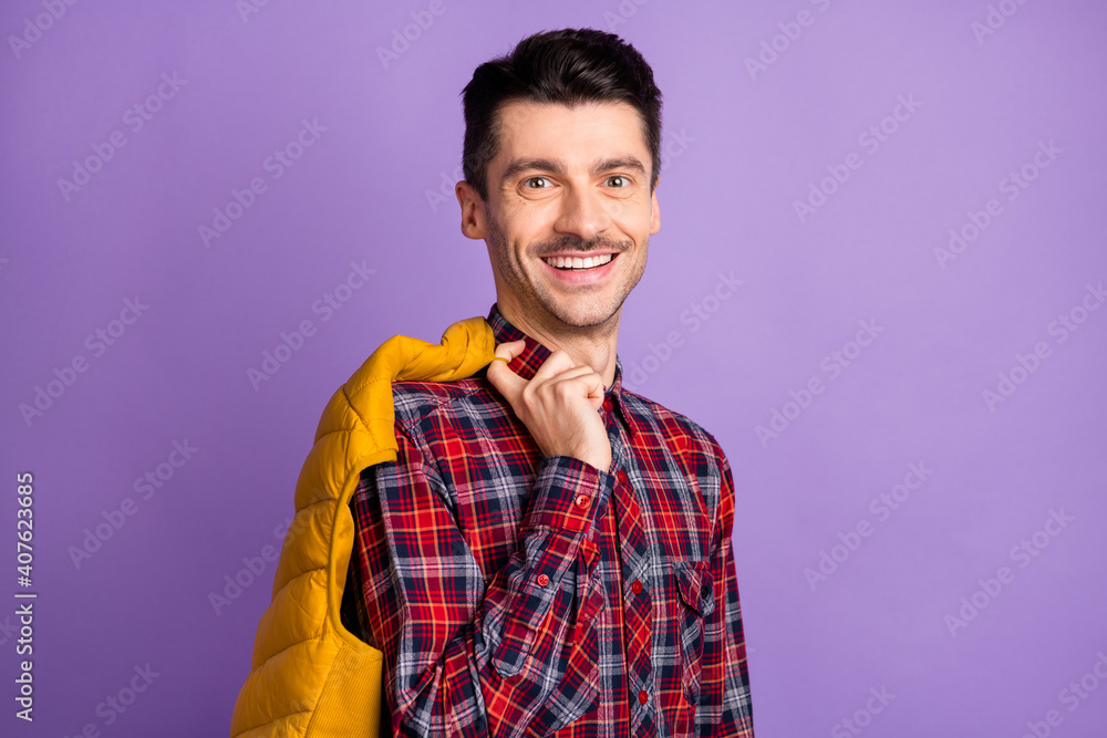 Photo of cheerful funny young guy dressed plaid shirt holding back yellow vest isolated purple color background