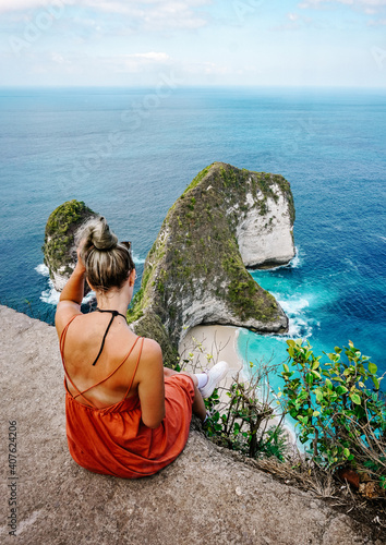 Young Woman sitting on a cliff and watching the ocean in Bali, indonesia. Enjoying the beautiful Kelingking beach which is shaped like a dinosaur in Nusa Penida. photo