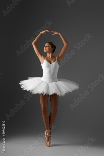 beautiful ballerina in white tutu and pointe shoes dancing on gray background