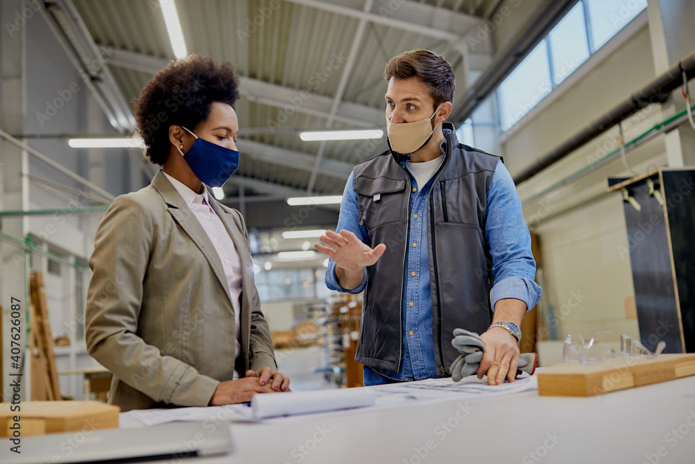 Woodworking foreman and female company manager communicating while examining design plans in a factory. Woodworking foreman and female company manager communicating while examining design plans in a factory.