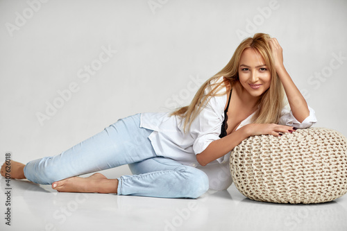 smiling beautiful blonde woman with long hair in jeans and white shirt sitting on floor