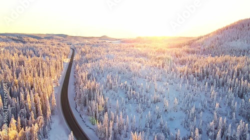 Cars driving on a highway in a  snow covered winter landscape at sunset.
