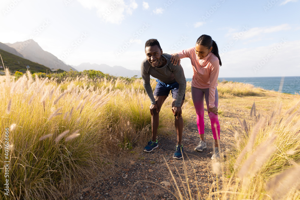 Fit african american couple in sportswear resting leaning on knees in tall grass