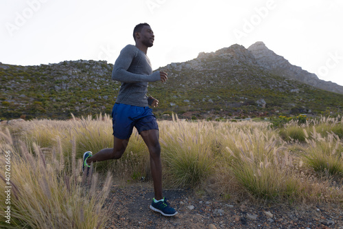 Fit african american man in sportswear running through tall grass