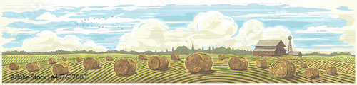 Autumn rural landscape in panoramic format with a farm and bales of hay in the foreground