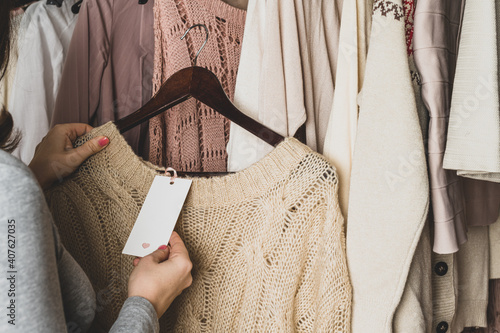 Woman shopper looking on tag  choosing  sweater from clothes in garment store. Shopping.