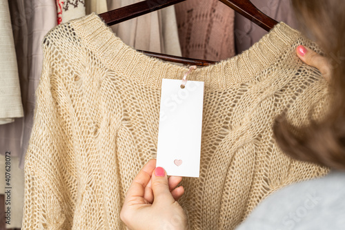 Woman shopper looking on empty tag, template choosing sweater from clothes in garment store. Shopping.