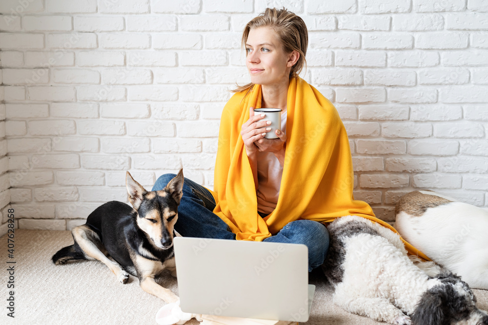 Funny young woman in yellow plaid sitting on the floor with her dogs drinking coffee