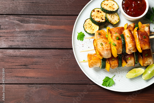 Delicious chicken shish kebabs with vegetables and sauce on wooden table, top view. Space for text