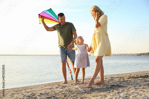 Happy parents with their child playing with kite on beach. Spending time in nature