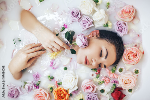 The woman takes a wellness bath filled with milk. The buds of multi-colored roses float on the surface. Relaxing and anti-aging treatments