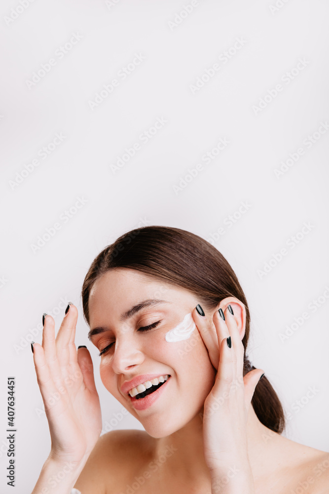 Attractive brunette enjoying spa procedure on isolated background. Smiling girl applies moisturizer Attractive brunette enjoying spa procedure on isolated background. Smiling girl applies moisturizer
