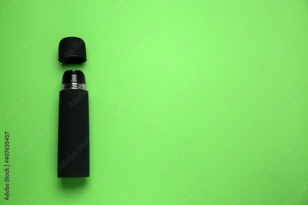 Black thermos and cup on green background, flat lay. Space for text Black thermos and cup on green background, flat lay. Space for text
