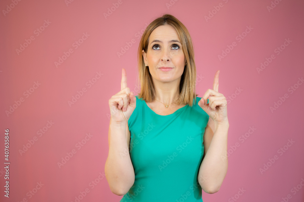 Young blonde woman wearing green dress over isolated background pointing fingers up with successful idea. Young blonde woman wearing green dress over isolated background pointing fingers up with successful idea.