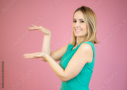Portrait of smiling woman showing something or copy space for product or sign text, isolated over pink background