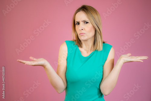 Young woman wearing green dress clueless and confused expression with arms and hands raised. Doubt concept.