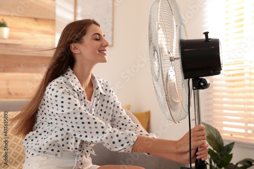 Quadro su tela Woman enjoying air flow from fan on sofa in living room