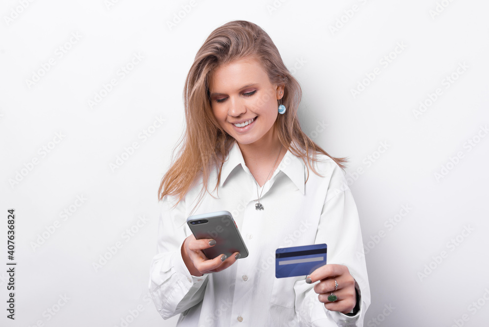Portrait of joyful young woman in white shirt using smartphone and blue credit card. Portrait of joyful young woman in white shirt using smartphone and blue credit card.