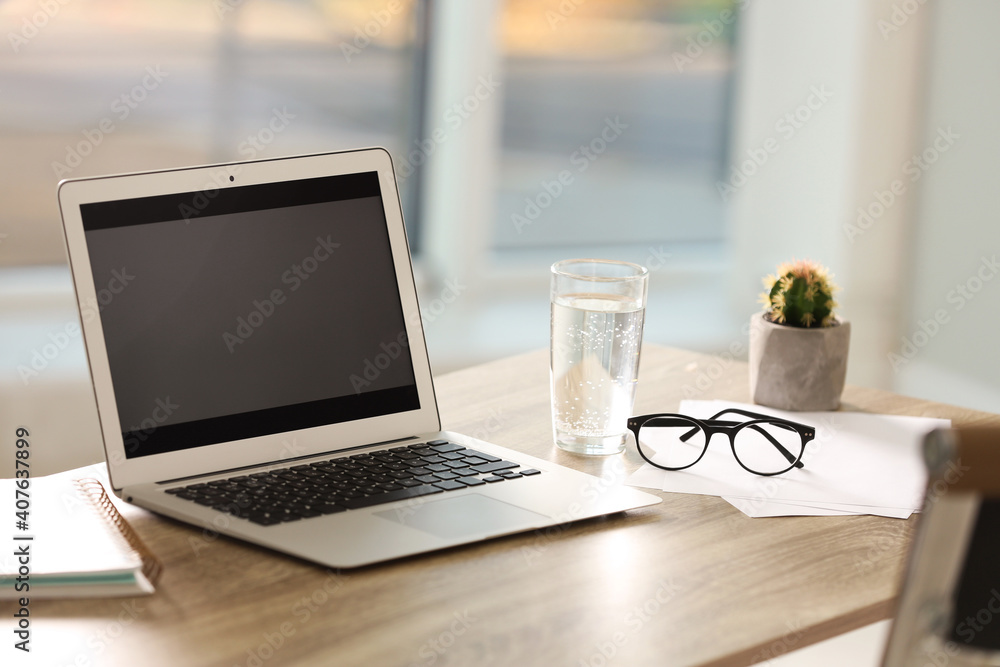 Fototapeta premium Modern laptop and glass of water on table in office