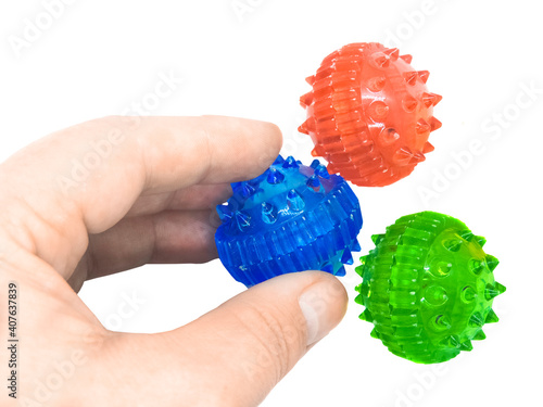 A hand picks up a blue massage ball from a pile of su jok therapy balls. Close-up movement is isolated on a white background. Development of fine muscles of the hand and motor skills of the fingers.