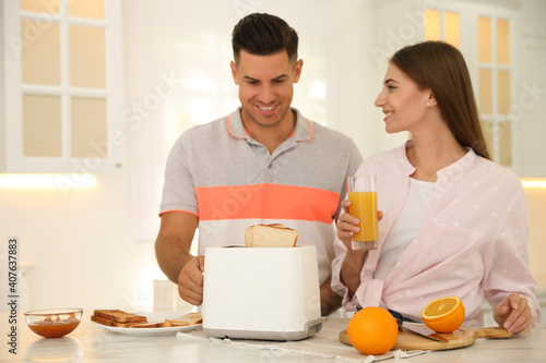 Happy couple preparing breakfast with toasted bread at table in kitchen