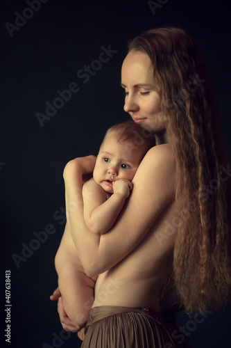 Beautiful long haired young woman is breastfeeding her cute tiny baby daughter in beautiful light. Image with selective focus, toning and noise effect.