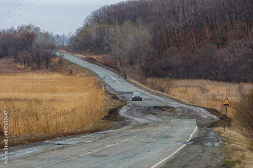 Bad Russian asphalt road. The asphalt road is full of holes and cracks among dried autumn trees. photo