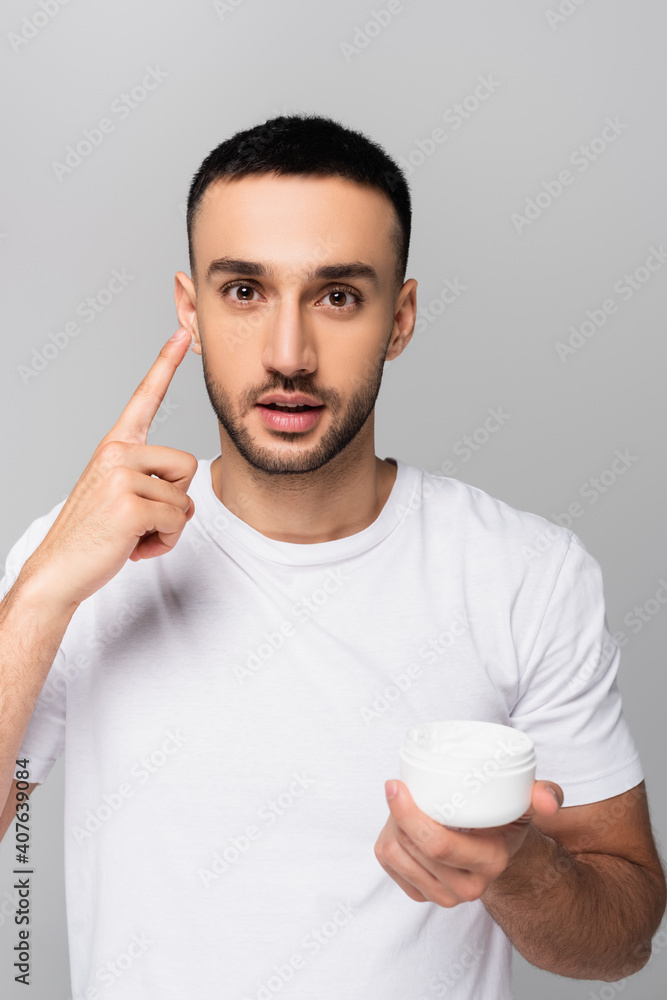 young hispanic man pointing applying face cream isolated on grey young hispanic man pointing applying face cream isolated on grey
