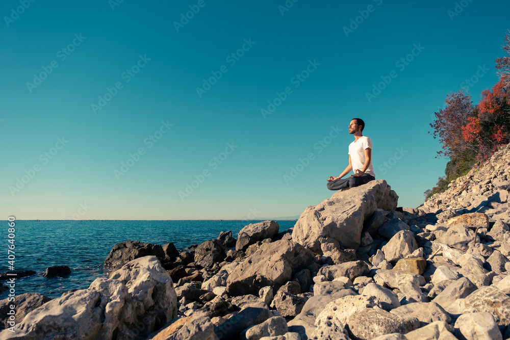 Obraz premium Attractive young man practicing yoga meditation and breathwork outdoors by the sea