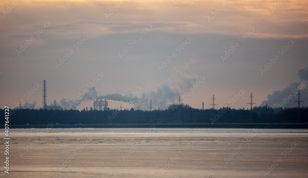 Smoke from chimneys of a metallurgical plant near a frozen lake